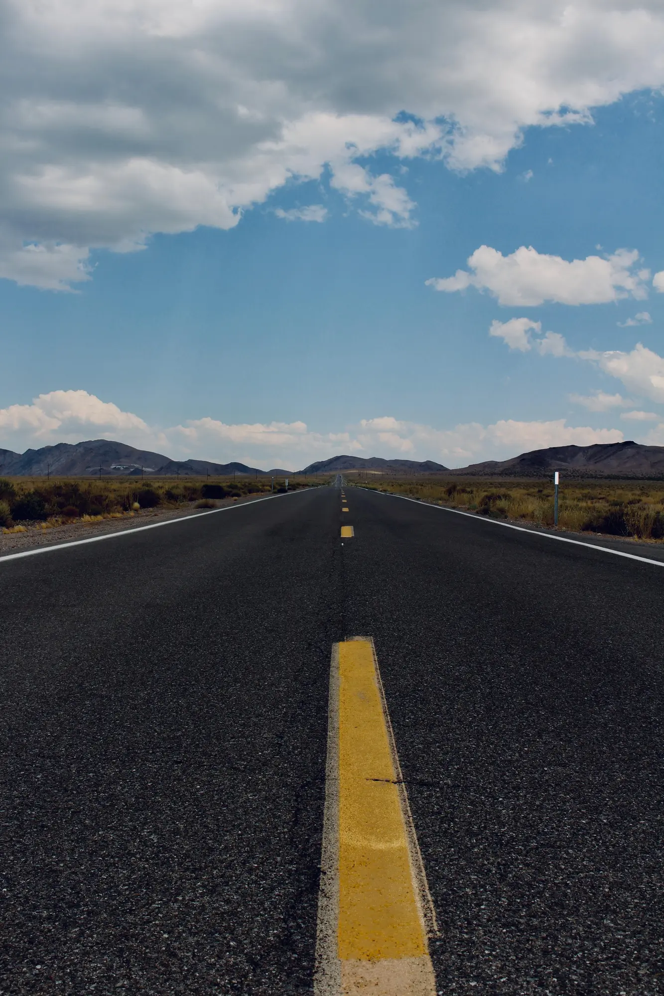 Straight road through Death Valley with mountains and clouds in the distance