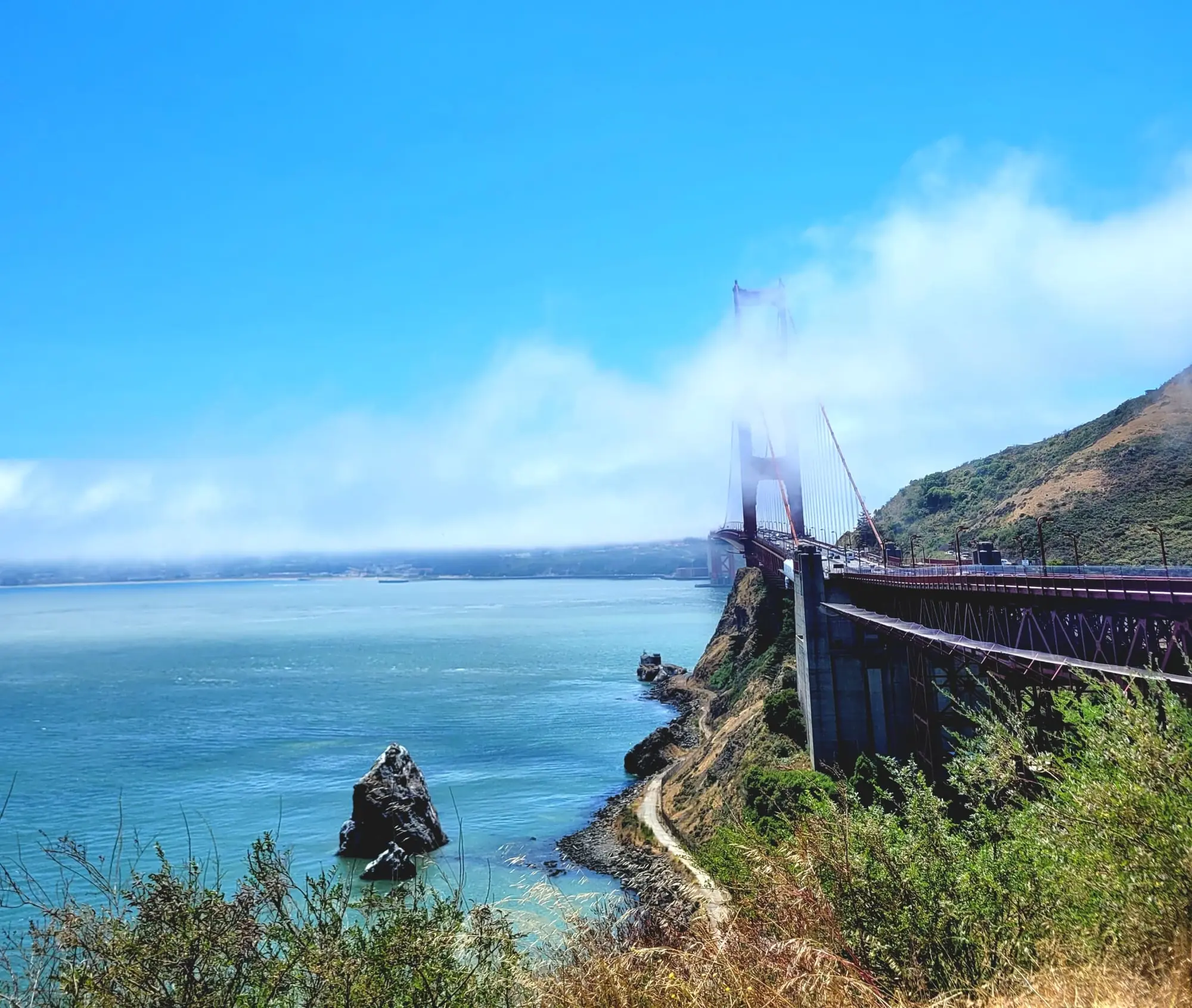 Golden Gate Bridge partly hidden in fog above the bay.