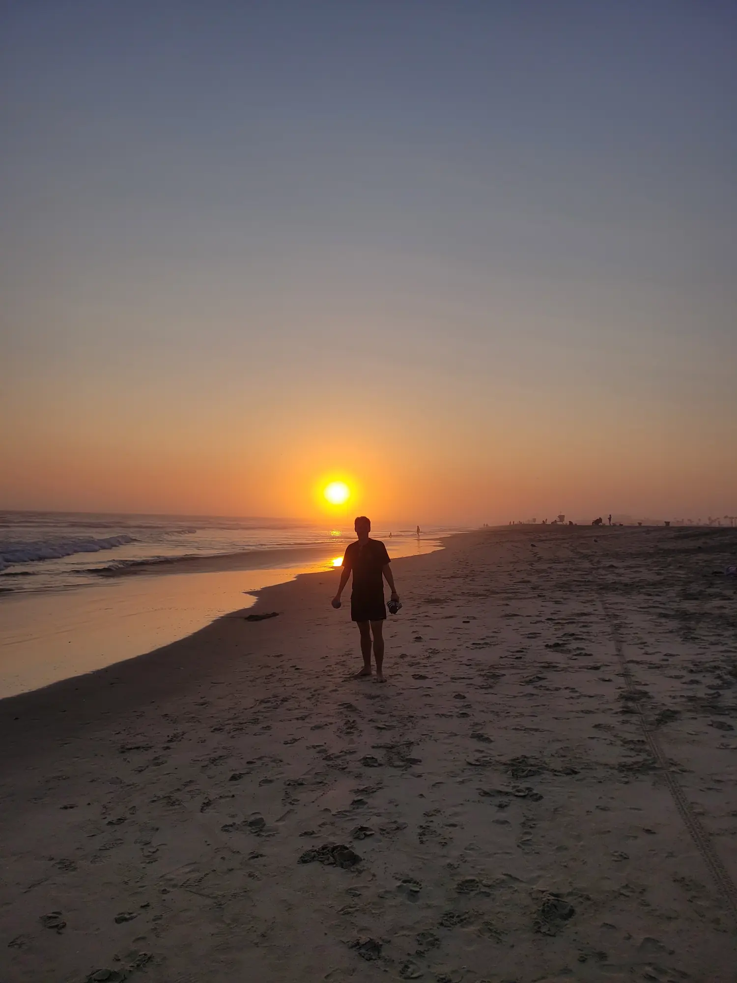 Person walking along Huntington Beach at sunset